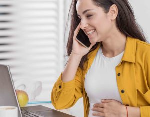 smiley pregnant woman talking phone with laptop ()